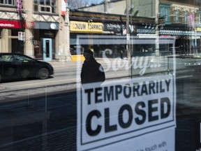 Storefronts in Ottawa's Glebe neighbourhood are reflected in a sign indicating the temporary closure of a business to prevent the spread of COVID-19, on Tuesday, March 24, 2020.