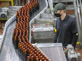 Hundreds of bottles of Budweiser flow past on the bottle line as a manager, Colin Suellentrop, looks on at Labatt Brewery in London earlier this month. Labatt is designating its products, including London-made Blue, Budweiser and Bud Light, Ontario Made as part of a provincial push to showcase Ontario businesses amid the COVID-clobbered economy. (Derek Ruttan/The London Free Press)