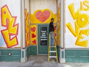 Rich Denomme has been hired by Farhi Holdings to paint over cladding erected to protect vacant storefronts in downtown London, and so far has painted about 8,000 square feet or about 300 sheets of plywood. (Mike Hensen/The London Free Press)