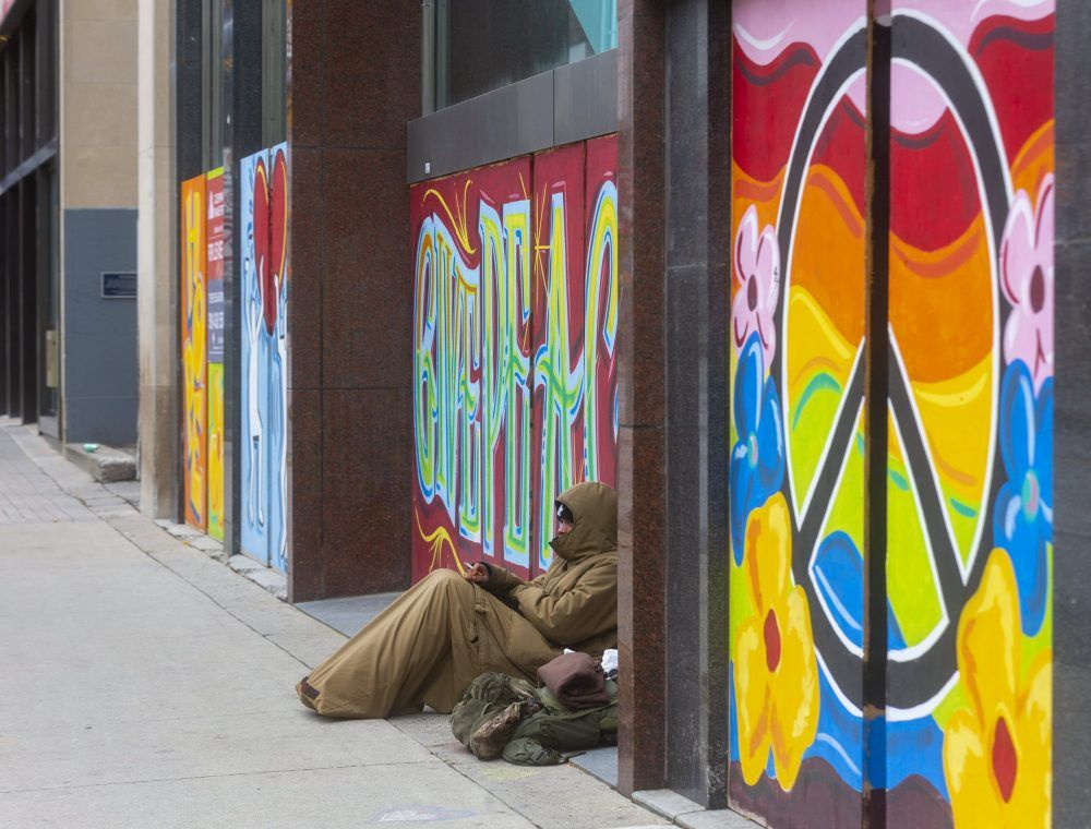 A homeless man rests on the artwork adorning an empty building on Richmond Street in London. (Mike Hensen/The London Free Press)