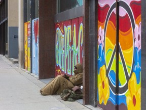 A homeless man rests on the artwork adorning an empty building on Richmond Street in London. (Mike Hensen/The London Free Press)