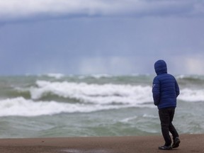 John Resendes of Cambridge battles the wind to watch white caps beat into the main beach at Grand Bend on Sunday. (Mike Hensen/The London Free Press)
