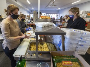 Conde de la ciudad Elizabeth Peloza, al frente a la izquierda, sirve pasta caliente mientras Tiffany Wilson-Walker de Old East Village Cares agrega la salsa con albóndigas mientras Tracey Sader, chef del St. Joseph's Hospitality Centre en Londres, apila comidas en Londres. Old East Village Cares se asoció con el centro de hospitalidad para producir cientos de comidas calientes para las personas que viven en la calle en el área. Fotografía tomada el 12 de noviembre de 2020. Mike Hensen/The London Free Press