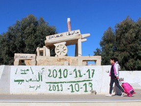 A girl walks past a memorial for Mohamed Bouazizi, a street vendor who set himself alight 10 years ago on December 17, 2010,  in Sidi Bouzid, Tunisia December 8, 2020. Graffiti reads: "The people want". Picture taken December 8, 2020. REUTERS/Angus McDowall