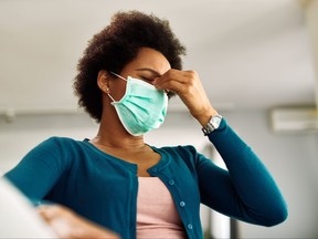 Below view of black woman with face mask having a headache at home.