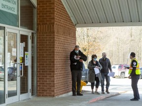 A security guard escorts two people waiting in line for their COVID-19 shots outside the Mt. Brydges vaccination centre west of London. (Mike Hensen/The London Free Press)