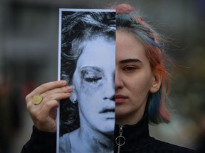 An activist of the "Declic" movement for women's rights holds a printed half face picture showing a victim of domestic violence during a protest in Bucharest on March 4, 2020, to draw attention to the lack of monitoring bracelets on the aggressors once a restraining order was issued.