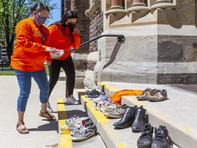Tammy Doxtator and her daughter Joelle Mandamin place tiny shoes on the steps of St. Peter's Cathedral Basilica in London on Sunday May 30, 2021. They were there for a memorial after 215 unmarked graves of children were discovered recently on the grounds of a former residential school in Kamloops, B.C. Doxtator's father was a residential school survivor and she said it's permanently affected their lives. The damage is "multi-generational . . . and we don't need more apologies, we need something to be done." (Mike Hensen/The London Free Press)
