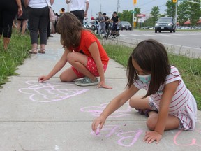 Ella Zadorsky-Hall, 5, (front) and Nyah Smith, 8, paint hearts on the sidewalk of Hyde Park Road on Tuesday night. They were among scores of Londoners who joined together to mourn four members of a local Muslim family killed in what police call a hate-motivated crime.  (JONATHAN JUHA/The London Free Press)