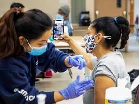 Ramona Ramos takes a selfie as a nurse from Humber River Hospital's mobile vaccine clinic administers a COVID-19 vaccine in Toronto. (REUTERS/Carlos Osorio)