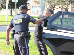 An OPP officer places a man in the back of a cruiser outside a townhouse complex near Notre Dame Drive and Viscount Road in London's Westmount area on Monday July 16, 2021. DALE CARRUTHERS / THE LONDON FREE PRESS