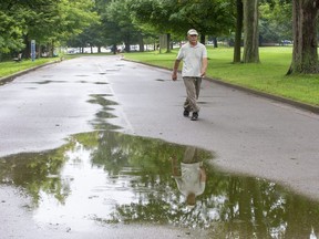 Mohamed Ali is reflected in a puddle as he goes for his daily walk through Springbank Park in London on Tuesda.  the hot, humid weather will break on the weekend, Environment Canada says. (Derek Ruttan/The London Free Press)