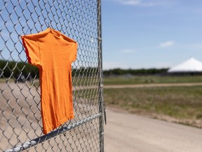 An orange shirt is seen on the gate of Enoch Park: Cree PowWow Grounds as fire keepers maintain a sacred fire in memory of 215 children found in unmarked graves at the closed Kamloops Indian Residental School at Enoch Cree Nation near Edmonton. Photo by Ian Kucerak