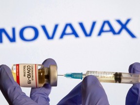 A woman holds a small bottle labeled with a "Coronavirus COVID-19 Vaccine" sticker and a medical syringe in front of displayed Novavax logo in this illustration taken, October 30, 2020. REUTERS/Dado Ruvic
