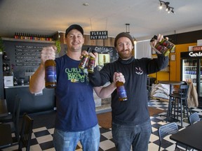 Curley Brewing Co. co-owner Nigel Curley, left, holds bottles of Space Time Galaxy IPA, while Proper Heathen Hot Sauce Co. owner Dave Ripley holds bottles of Space Time Heat Green Curry IPA hot sauce he created with Curley's brew. (Derek Ruttan/The London Free Press)