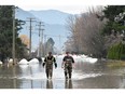 Two workers walk through floodwater after conducting a hazard assessment at a local bio gas plant in Abbotsford after rainstorms lashed British Columbia, triggering landslides and floods.