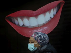 A pedestrian wearing a mask walks past an animated smiling mouth and teeth out front of Dorval Dental on Toronto's Bloor Street West during the COVID 19 pandemic in Toronto, on Dec. 14, 2021.