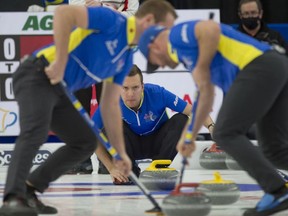 Alberta skip Brendan Bottcher crouches in the rings as lead Karrick Martin and third Darren Moulding brush the stone into the house at the 2021 Brier curling championships in Calgary. (File photo)