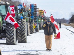 A man paces up and down the line of 18 farm vehicles parked on Highway 402 at the Forest Road exit in Lambton County on Sunday, Feb. 13, 2022. On Thursday, there were 20 vehicles. The westbound lanes are closed between Nauvoo Road and Forest Road. (Derek Ruttan/The London Free Press)