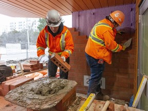 Bricklayers Tayler Wareham and Aaran Dignard from Render Construction work near the front entrance of an under-construction apartment building at 122 Base Line Rd in London. The building is a modular housing project, one of three city-led rapid builds aiming to help ease the housing crisis. (Mike Hensen/The London Free Press)