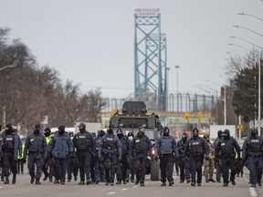 A large police force marches south on Huron Church Road, clearing protesters that have blockaded the road since last Monday, on Sunday, February 13, 2022.
