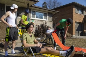 Adorned with two Irish flags, Andrei Merkulov holds a beer as he soaks up the sun with his housemates Thursday morning on the lawn of their Huron Street home. (Mike Hensen/The London Free Press)