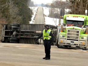A delivery truck lays on its side on Perth Road 112 in the Stratford-area village of Harmony after colliding with a transport truck at the road’s intersection with Perth Line 26 just before 9:30 a.m. Tuesday March 1, 2022. A Stratford police auxiliary officer directs traffic as tow truck operators worked to clear the road. (Galen Simmons/Postmedia Network)