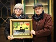 Former London restaurant owners Irene and Tony Demas hold a Maud Lewis painting they received decades ago from a regular customer in exchange for steady supply of grilled cheese sandwiches. The painted fetched $350,000 in an auction Saturday. (Contributed/Miller and Miller Auctions)