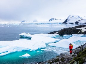 Tourist taking photos of amazing frozen landscape in Antarctica with icebergs, snow, mountains and glaciers, beautiful nature in Antarctic Peninsula.