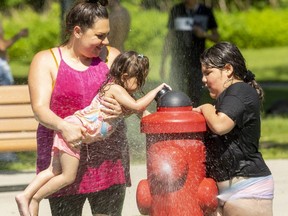 Rachel Cole holds up her youngest daughter, Lily Clause, 2,  so she can hit the switch with her oldest daughter, Everleigh Clause, 7, as they enjoy the cooling waters of the Gibbons Park splashpad in London on Tuesday, June 14, 2022. (Mike Hensen/The London Free Press)