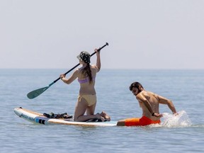 Verity Shatkin, gets a bit of an assist from her boyfriend Tegbir Lai, as they double up on a standup paddle board off the main beach in Port Stanley on Friday June 24, 2022. (Mike Hensen/The London Free Press)