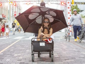 Amy  Agostina and daughter Mia , 7, stay dry while Junior Agostina pulls them in a wagon during Canada Day celebrations at Dundas Place in London, Ont. on Friday, July 1, 2022.  (Derek Ruttan/The London Free Press)