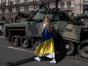 A woman wrapped in the Ukrainian flag walks among damaged Russian military vehicles set up in downtown Kyiv on Aug. 24, Ukraine's independence day, The day commemorating its break with the Soviet Union in 1991, coincides with the six-month mark since Russia invaded. (Alexey Furman/Getty Images)