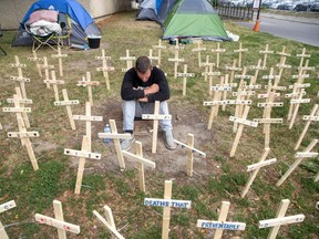 Jason Joyce sits among 167 crosses outside of London's city hall on Wednesday, Aug. 3, 2022. The crosses represent each homeless person who has died in the past three years. They are placed beside a tent where Dan Oudshoorn is staging a hunger strike to back a coalition's demands for changes to London's approach to homelessness. (Derek Ruttan/The London Free Press)