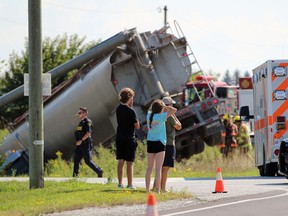 Three people look on in distress as Lambton County firefighters, police and paramedics respond to a crash at the intersection of Inwood Road and Courtright Line in Brooke-Alvinston on Tuesday Aug. 23, 2022. (Terry Bridge/Postmedia Network)