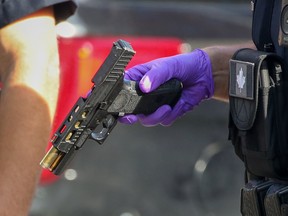 A Calgary police officer holds a pellet/airsoft gun after it was ditched by a fleeing suspect on June 20, 2022. (Postmedia)