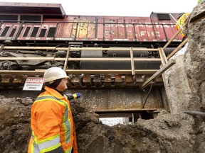 Steve Thynne, site superintendent for McLean-Taylor Construction, stands in an early excavation on Tuesday, Dec. 20, 2022, and watches as a CP Rail engine begins to cross one of the four small rail bridges built by the contractor at the site of the future Adelaide Street rail underpass in London. (Mike Hensen/The London Free Press)