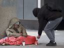 Un vagabundo intenta calentarse mientras un transeúnte le da algo de cambio.  Tony Caldwell/Postmedia