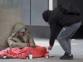 A homeless man tries to stay warm while a passerby gives him some change. (Tony Caldwell/Postmedia Network)