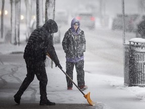 A shop owner shovels the sidewalk in Windsor while a pedestrian walks past during a significant snow storm on Wednesday, Jan. 25, 2023.   (DAX MELMER/Windsor Star)