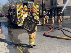 A firefighter carries the Black Walnut sign away while crews douse the Wortley Road cafe following an overnight fire that caused more than $1 million damage on Sunday April 16, 2023. Dale Carruthers / The London Free Press