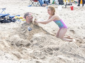 Dayla Delorme (8) of London buries her father Shawn in the sand at the beach in Grand Bend on Monday May 22, 2023. Photo by Derek Ruttan/The London Free Press