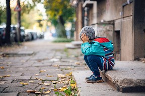 Little boy sitting alone and sad on the street