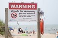 Several people take a dip in Lake Huron despite a warning sign posted at Grand Bend's south beach on Sunday July 16, 2023. (Derek Ruttan/The London Free Press)