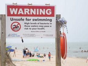 Several people take a dip in Lake Huron despite a warning sign posted at Grand Bend's south beach on Sunday July 16, 2023. (Derek Ruttan/The London Free Press)
