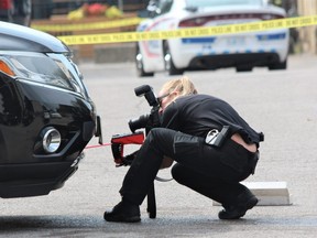 London police forensic investigator photographs a suspected bullet hole in an SUV