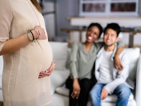 Pregnant Woman Touching Her Belly Standing In Front Of Smiling Young Couple