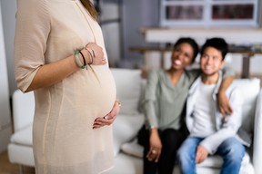 Pregnant Woman Touching Her Belly Standing In Front Of Smiling Young Couple