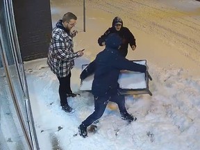 Screenshot of three guys on surveillance camera, with one picking up planter and about to throw it through window of business in Quinte West, Ont.