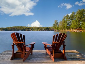 Two Adirondack chairs on a wooden dock facing a lake